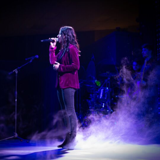 A singer performs on stage, there is dry ice fog around their feet.